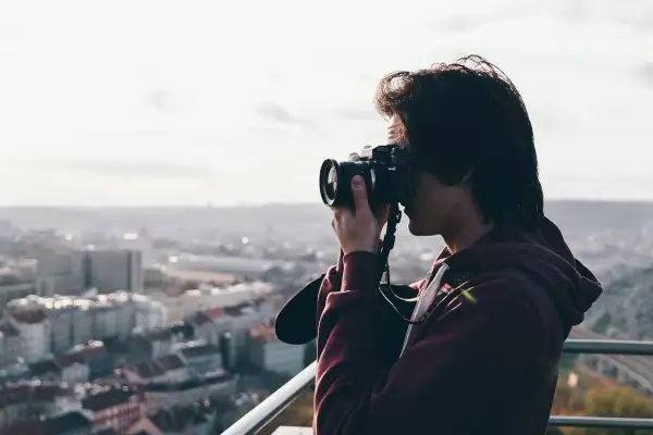 Przeswietlone zdjecie. Młody mężczyzna z aparatem fotograficznym w rękach, robiący zdjęcie miasta z góry.