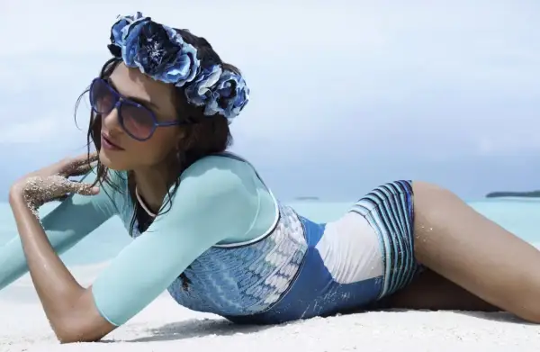 Kobieta w kwiecistej opasce i okularach leży na plaży. Idealne zdjecia na plazy inspiracje dla każdej kobiety.