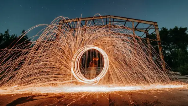 Nocna fotografia z kręcącym się ogniem tworzącym świetlisty okrąg. To definicja kreatywnej fotografii.