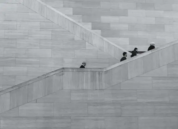 Ludzie idący po schodach, minimalistyczna kompozycja. Świetny przykład do poradnika fotograficznego o kompozycji i kadrze.