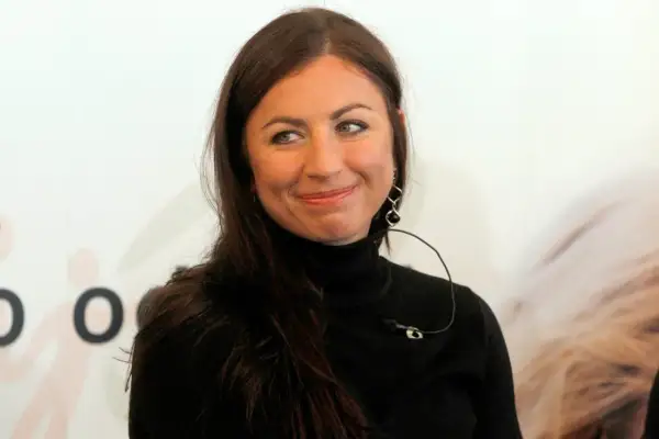 Uśmiechnięta Diana Kowalczyk w czarnym golfie, z charakterystycznymi kolczykami, patrzy w bok.